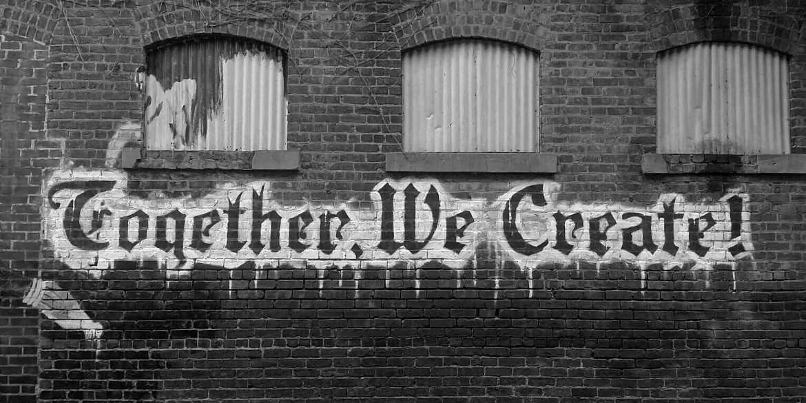 Black and white image of graffiti on a wall. Graffiti says "together, we create"