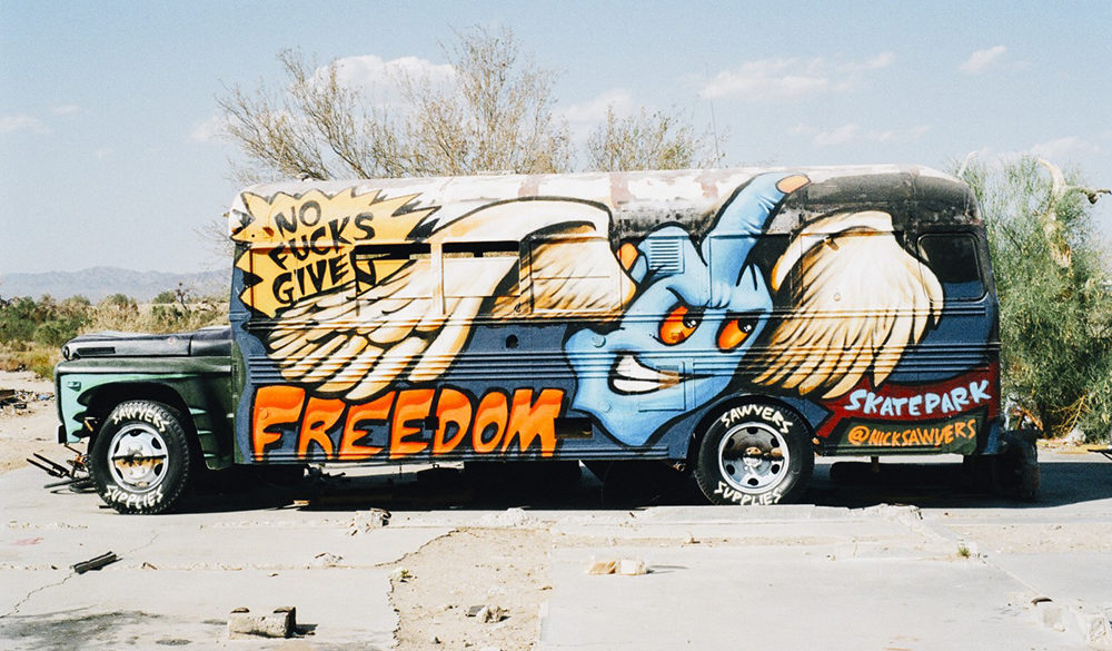 Old bus with graffiti flying middle finger hand and the word 'freedom'