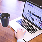 Open laptop with one hand typing, the other holding coffee