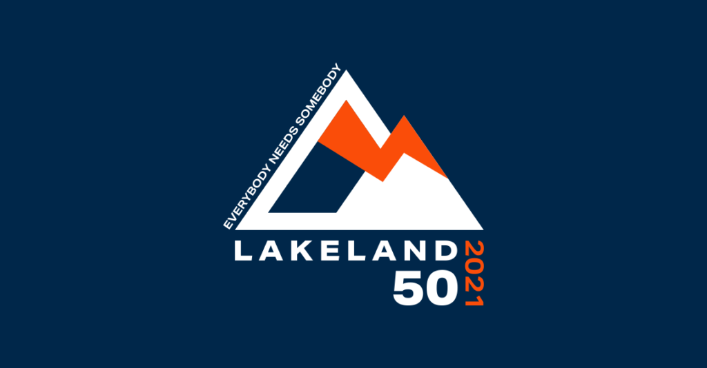 Logo depicting two mountains, one slightly smaller than the other front. Lightening bolt joins the two. Text up the left of left mountain reads "everybody needs somebody". Text below reads Lakeland 50 2021.