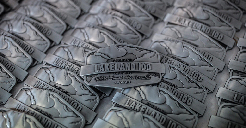 Image shows the Lakeland 2023 100 distance belt buckle logos.