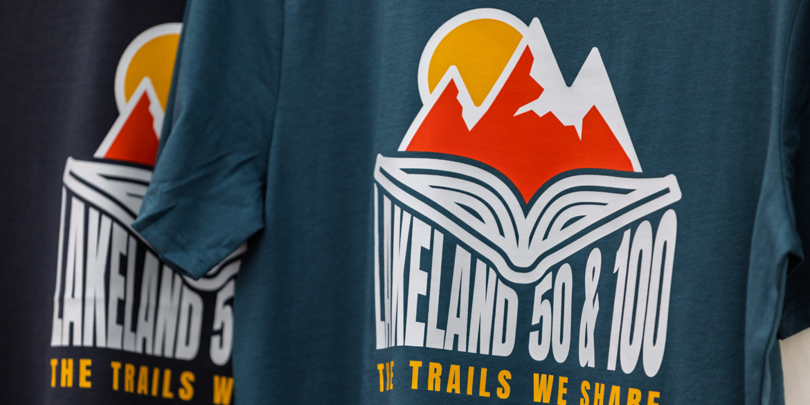 Lakeland 50 & 100 finisher t-shirts printed with the Lakeland 2025 event logo design featuring mountain, sun, and storybook illustration.